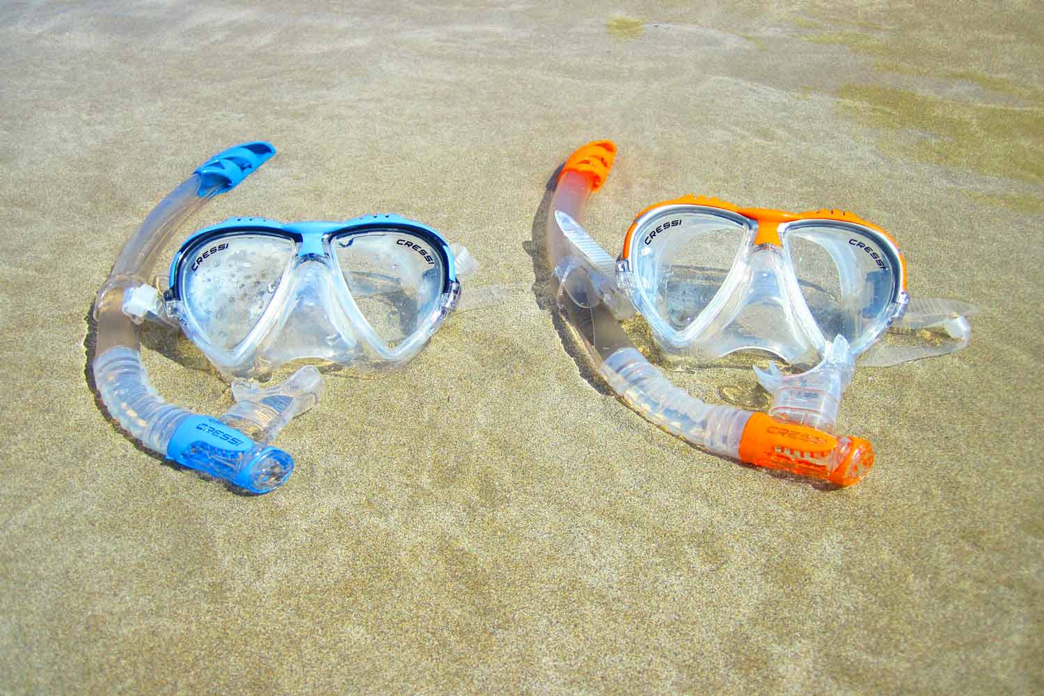 Zwei bunte Taucherbrillen liegen am Strand im Wasser