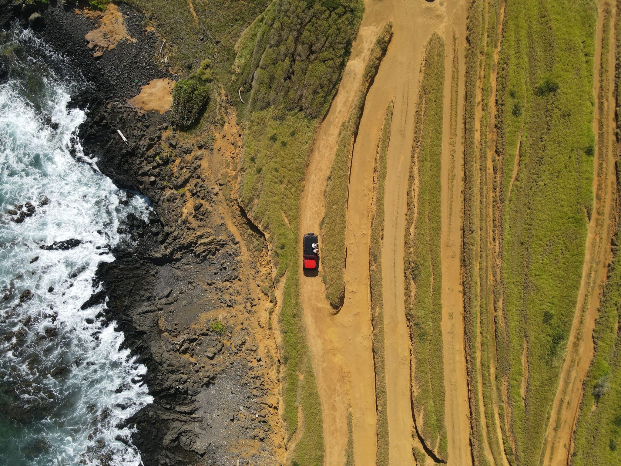Roter Jeep auf einer Sandpiste an der Küste von Hawaii, von oben